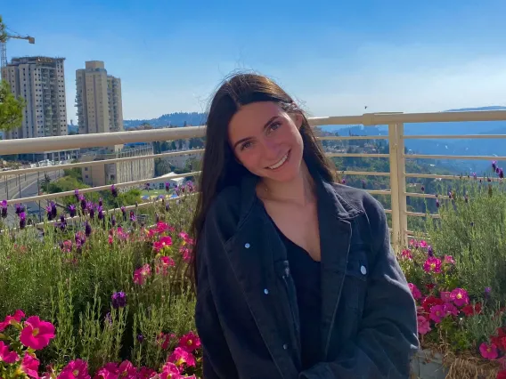Person with long brown hair smiling with blue sky and red flowers in the background.