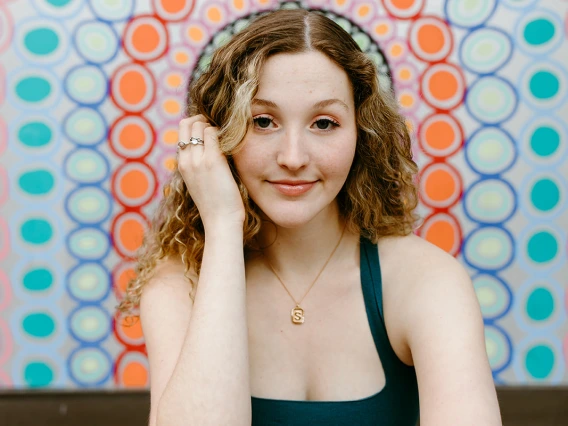 Photo of person with long red/blonde curly hair and colorful background.