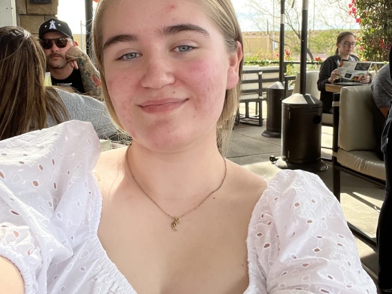 Person with white shirt and gold necklace with blond hair and blue eyes.