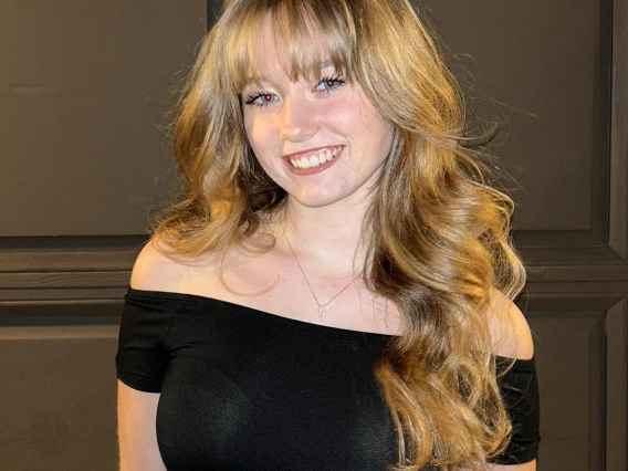 Person with long blonde hair and blue eyes and black top smiling