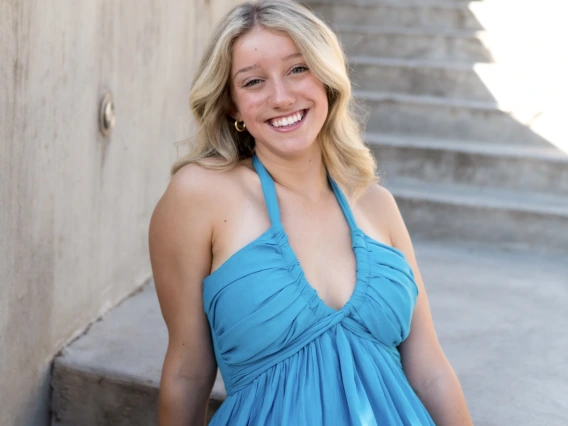Person with long blonde hair and blue dress smiling