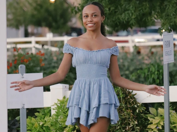 Person with blue dress and black sandals smiling with hands out.