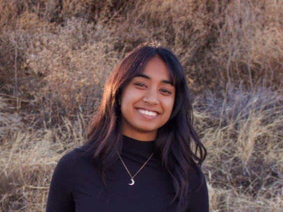 Person with long black hair and crescent moon necklace and black turtle neck smiling