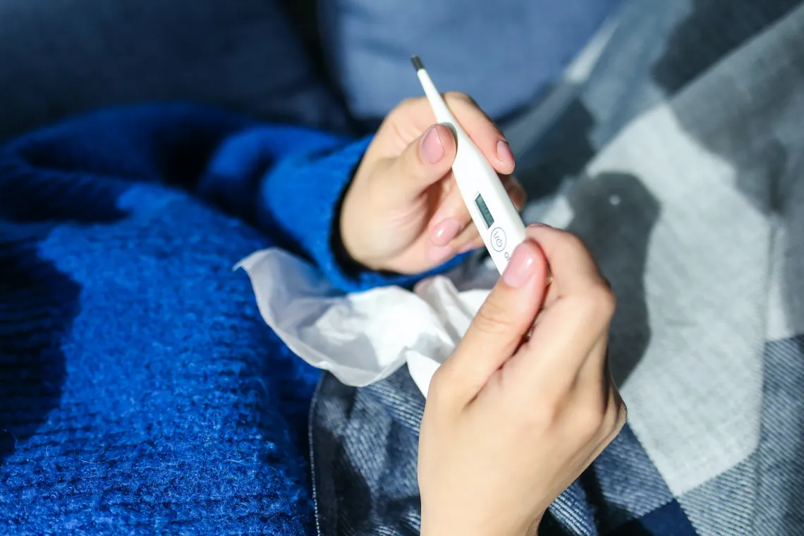 Hands holding a thermometer with a tissue resting on person's stomach